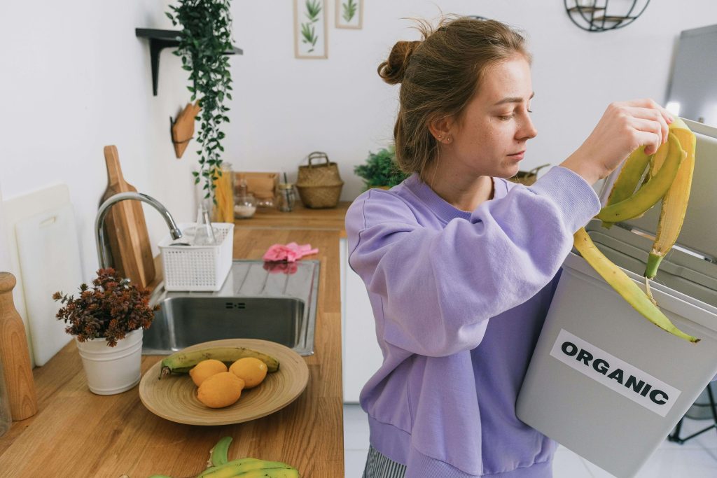 Woman adding chopped vegetable peels to her home compost pot in the kitchen